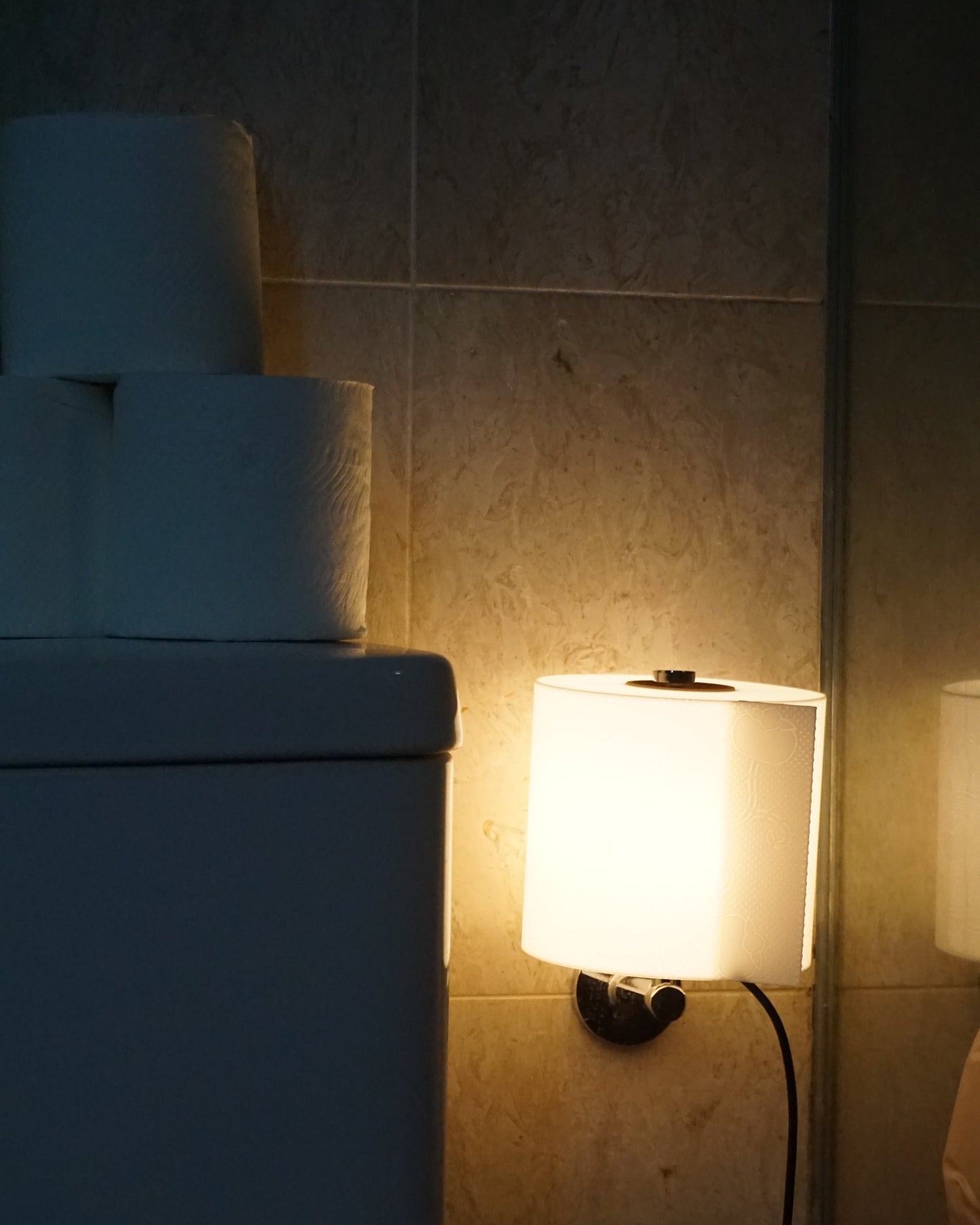 Illuminated toilet paper lamp hanging directly from a standard wall-mounted toilet paper holder