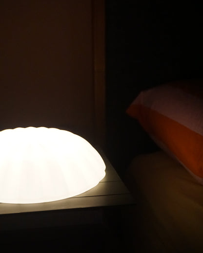 Illuminated Kueh Tutu lamp placed on a bedside table, casting a gentle, warm glow onto the pillow, bed and headboard