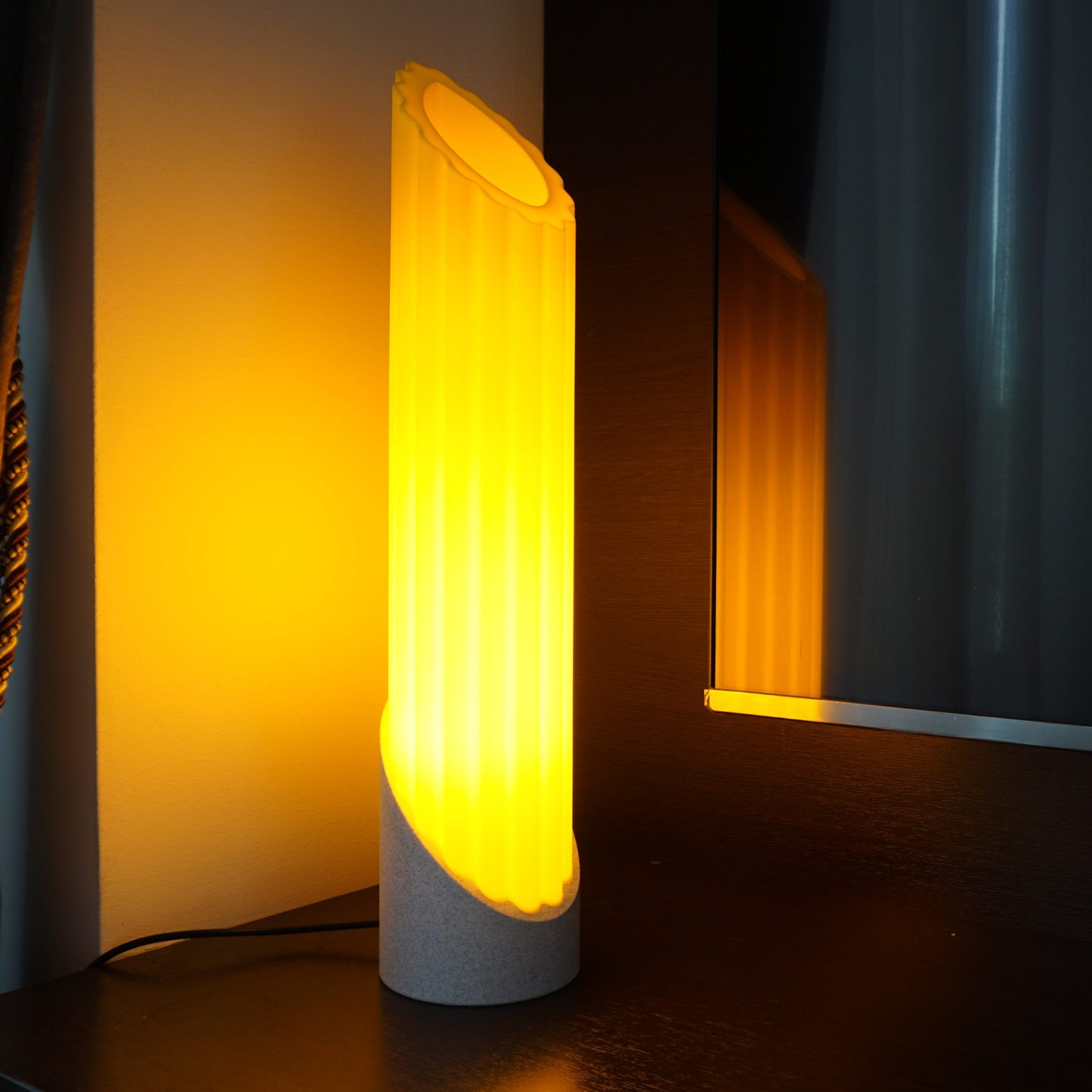 Illuminated Penne Pasta lamp at the corner of a TV console, casting a warm glow with a subtle reflection on the edge of the TV screen