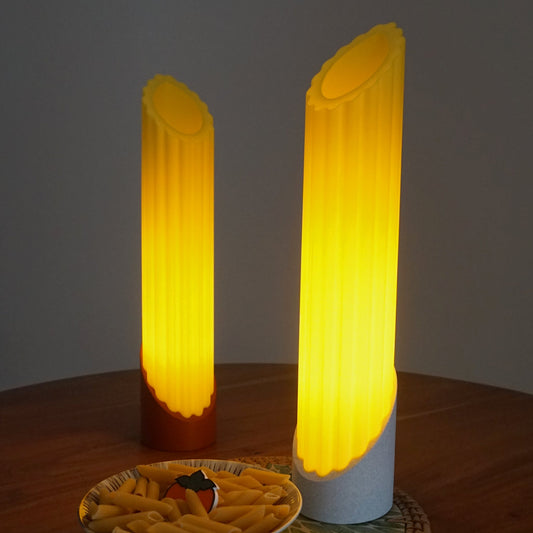 Two Penne pasta lamps glowing warmly, styled alongside a bowl of pasta, on top a mini persimmon logo