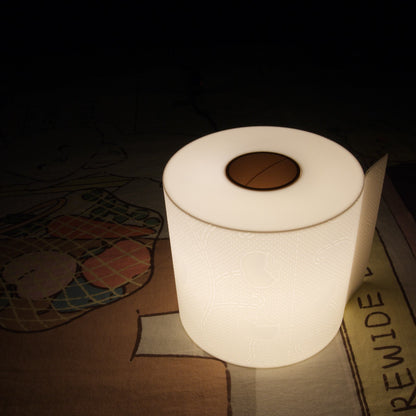 Illuminated toilet paper lamp glowing in complete darkness while resting on a bed, highlighting its soft ambient light