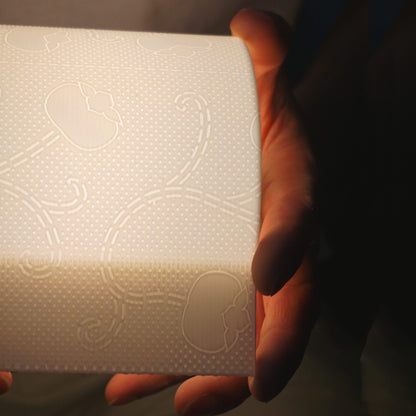 Illuminated toilet paper lamp held horizontally, showing its full side profile and casting a gentle, uniform glow