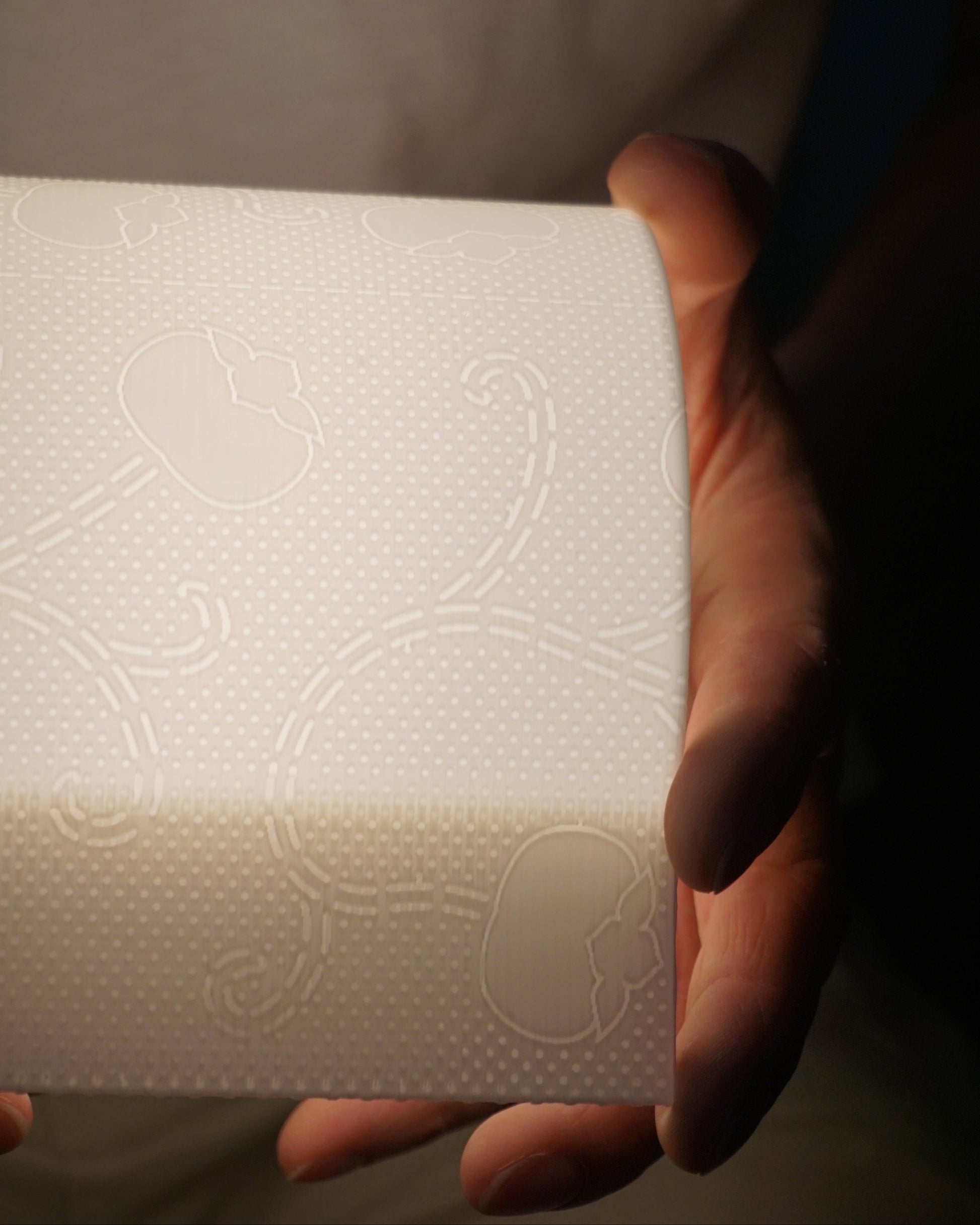 Illuminated toilet paper lamp held horizontally, showing its full side profile and casting a gentle, uniform glow